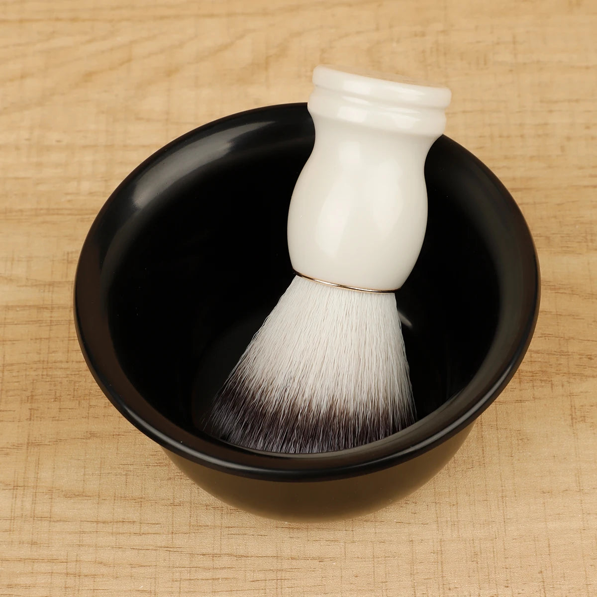 White shaving brush with black bristles in a black bowl on a wooden surface