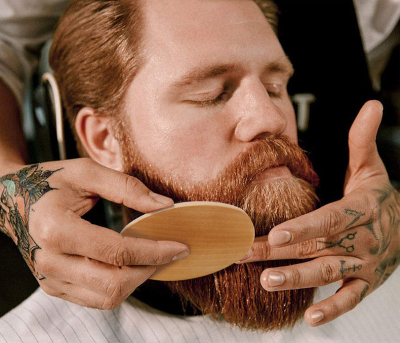 Man with tattoos grooming his beard with a wooden brush