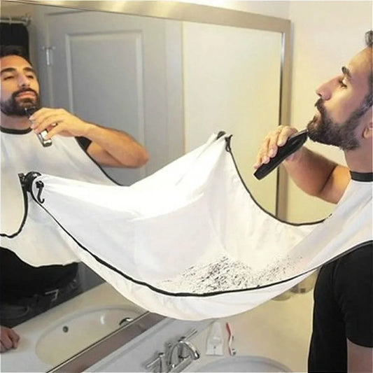 Man using a beard trimmer with a white bib to protect his clothes in front of a mirror.