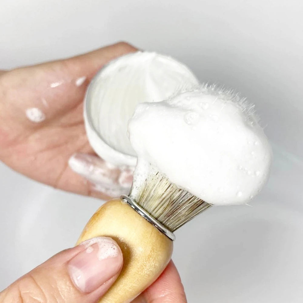 Hand holding a shaver brush with white shaving cream on a plain background