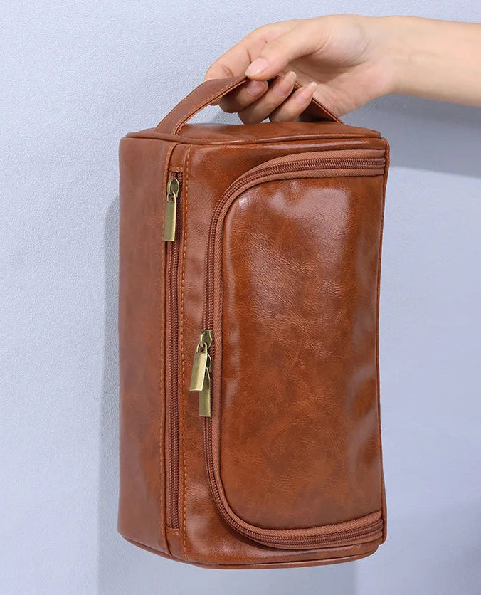 Brown travel bag with gold zippers held by a hand against a light gray background