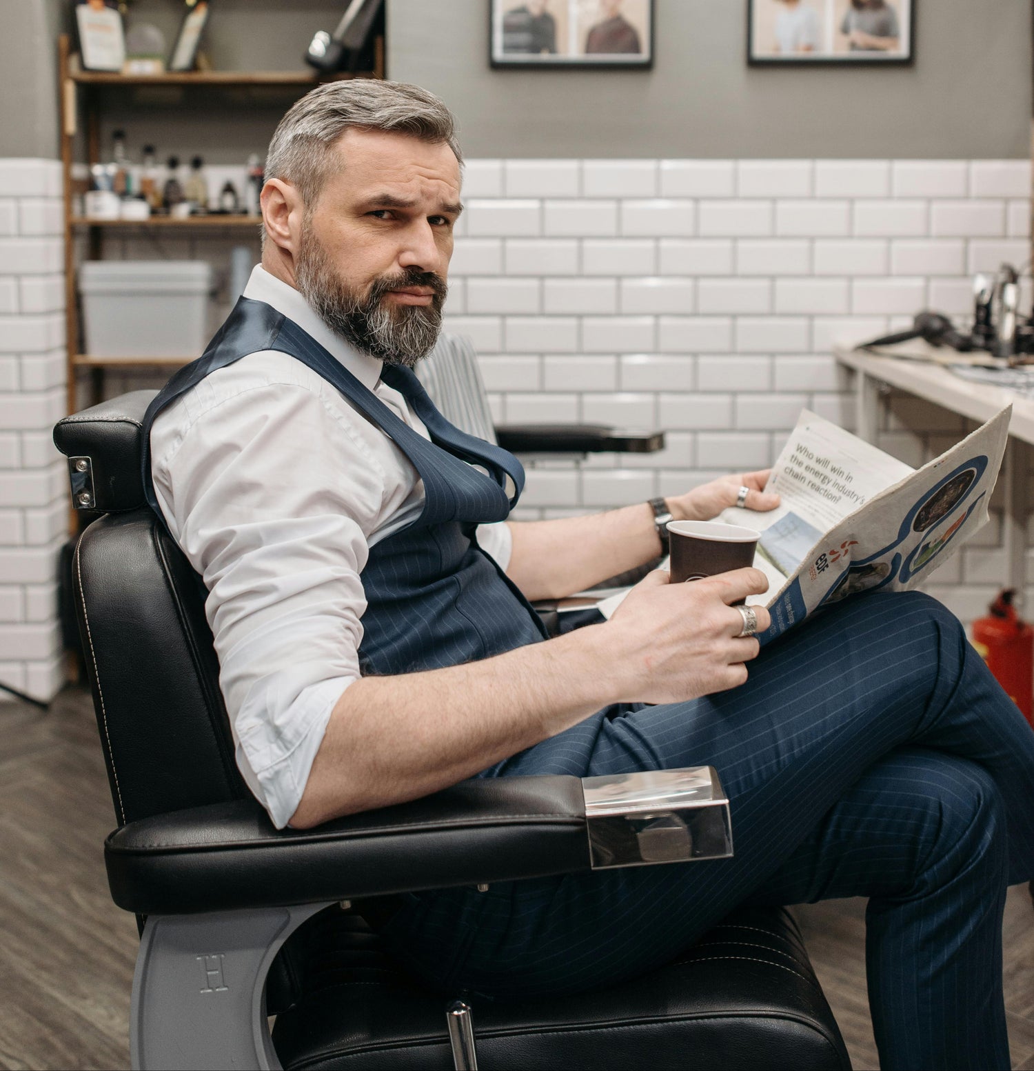 Man sitting in a barber chair reading a magazine in a barbershop.